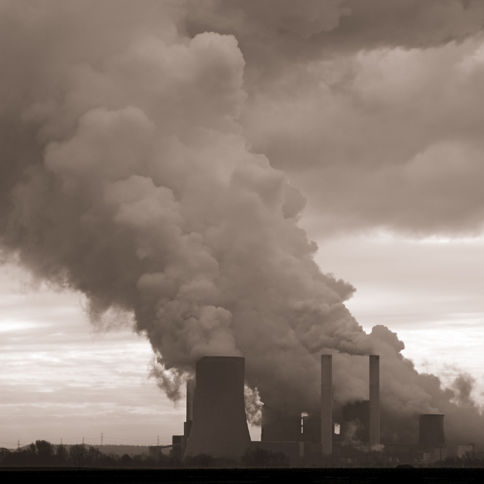 Chimneys spew pollution against a cloudy sky